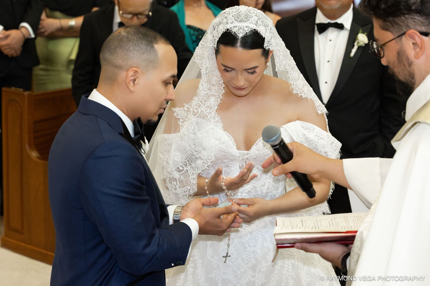 Bride and groom exchange rings at church altar during elegant wedding ceremony, bride wearing lace gown and veil.