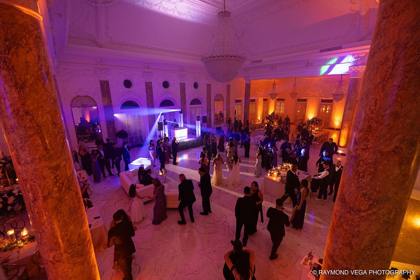 Elegant grand hall event venue with purple and amber uplighting, guests mingling on marble floors beneath tall columns.Antiguo Casino Puerto