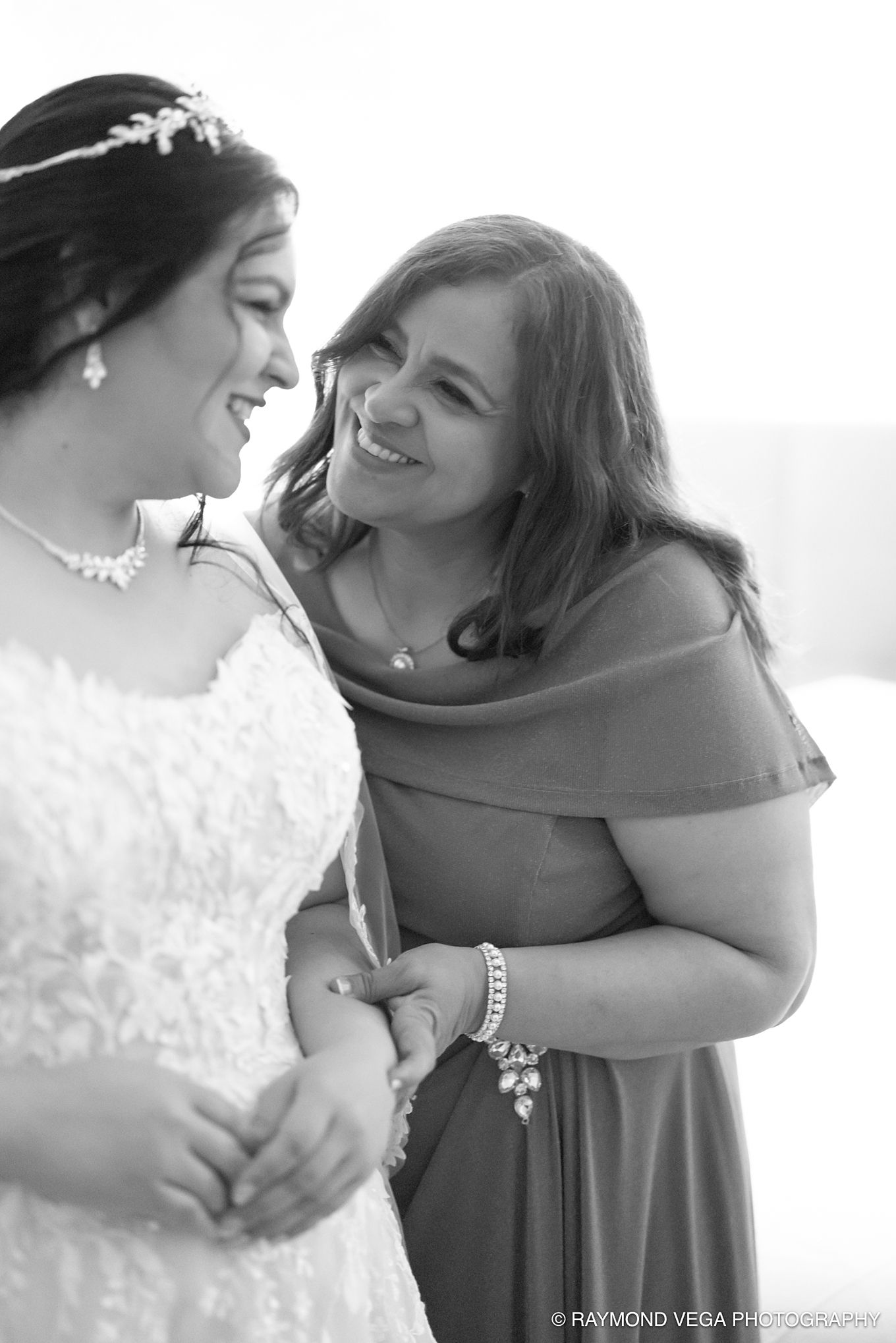 Black and white photo of a smiling bride and woman in off-shoulder dress sharing a joyful moment at a wedding.