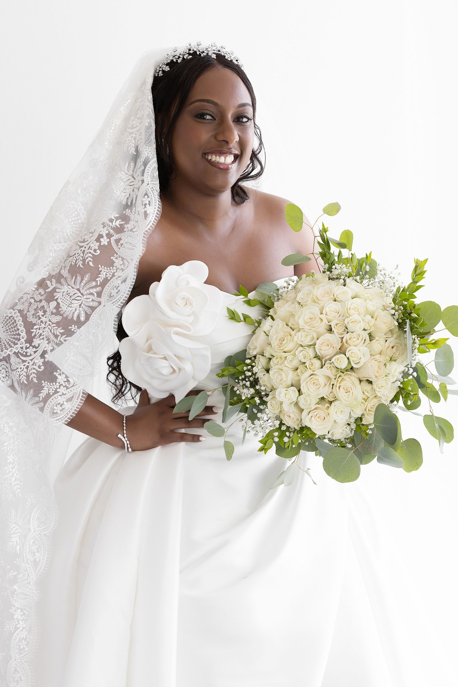 Smiling Black bride in white strapless gown and lace veil holding large bouquet of white roses and greenery. Hotel La Concha Puerto Rico