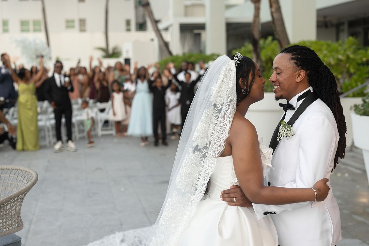 Bride and groom share a romantic moment at outdoor wedding ceremony with cheering guests in background. Hotel La Concha Puerto Rico
