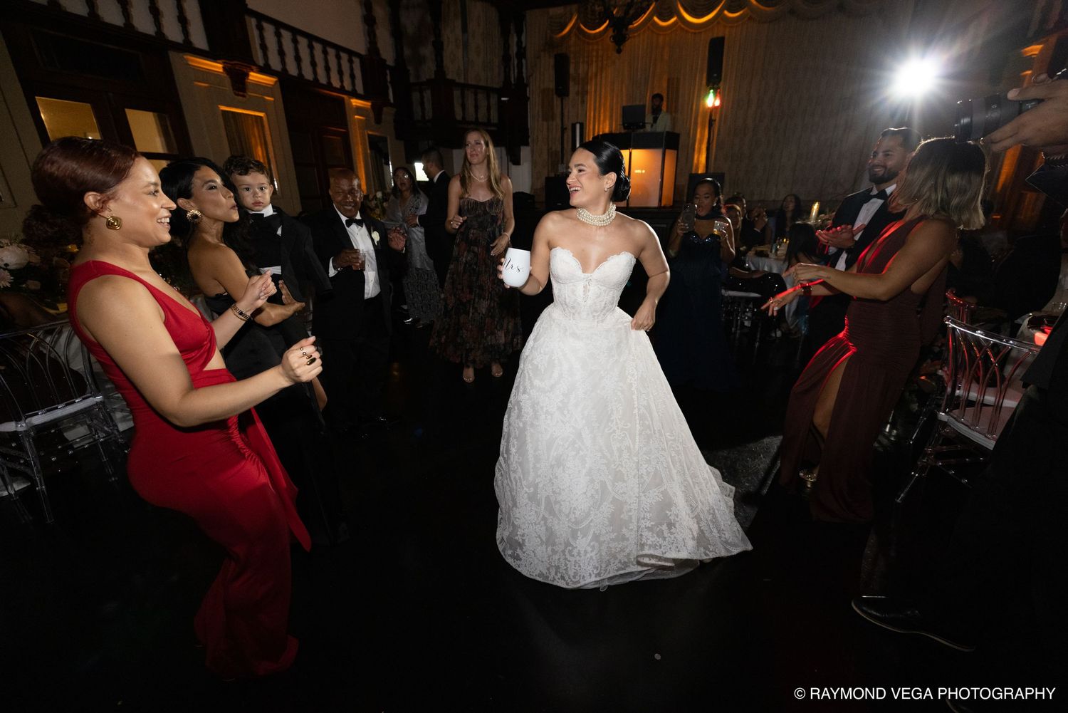 Bride in white ball gown dancing with guests at elegant wedding reception while string musicians perform nearby.