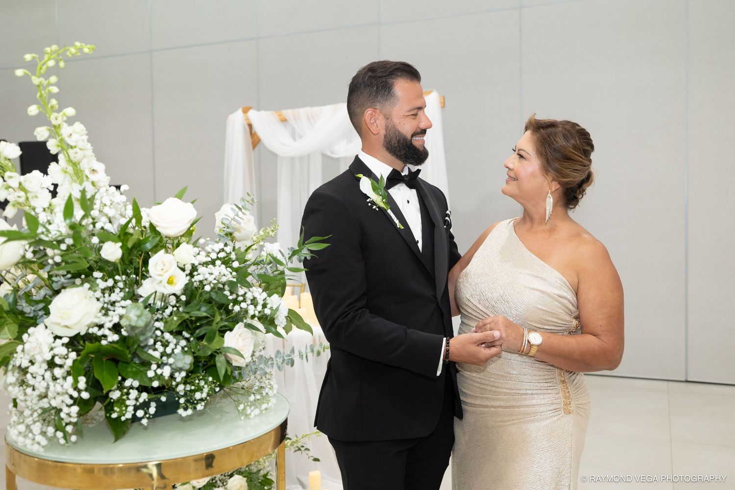Bride and groom share a joyful moment at their elegant wedding ceremony surrounded by white floral arrangements.
