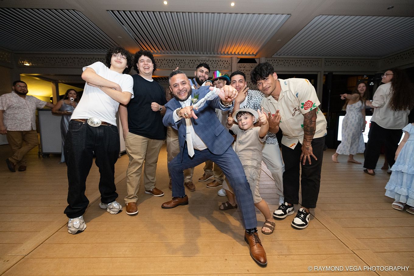 Group of men celebrating at a wedding reception, posing energetically on the dance floor in formal and casual attire at Courtyard by Marriot