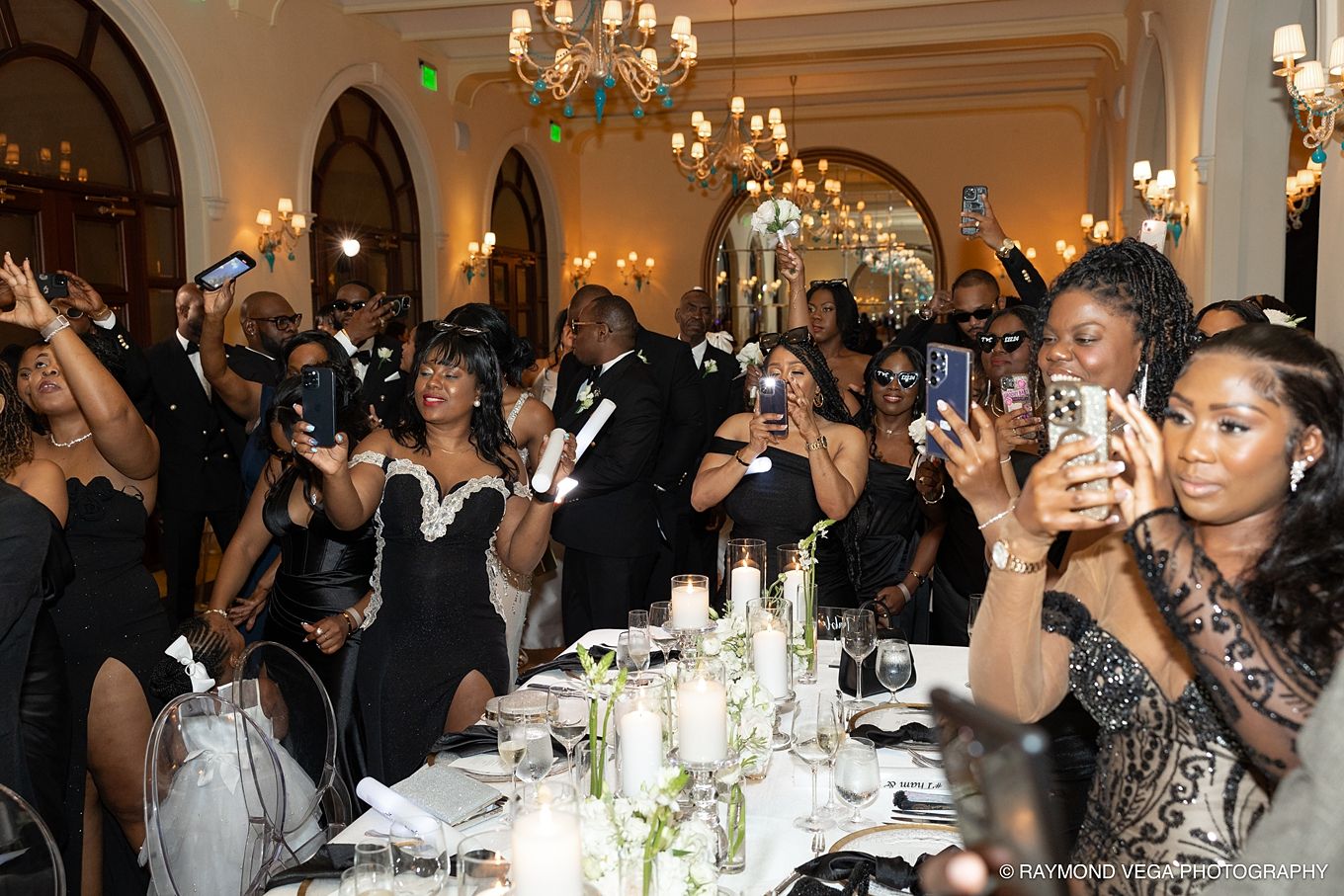 Elegant black-tie gala with guests in formal attire photographing a celebration in a grand ballroom.