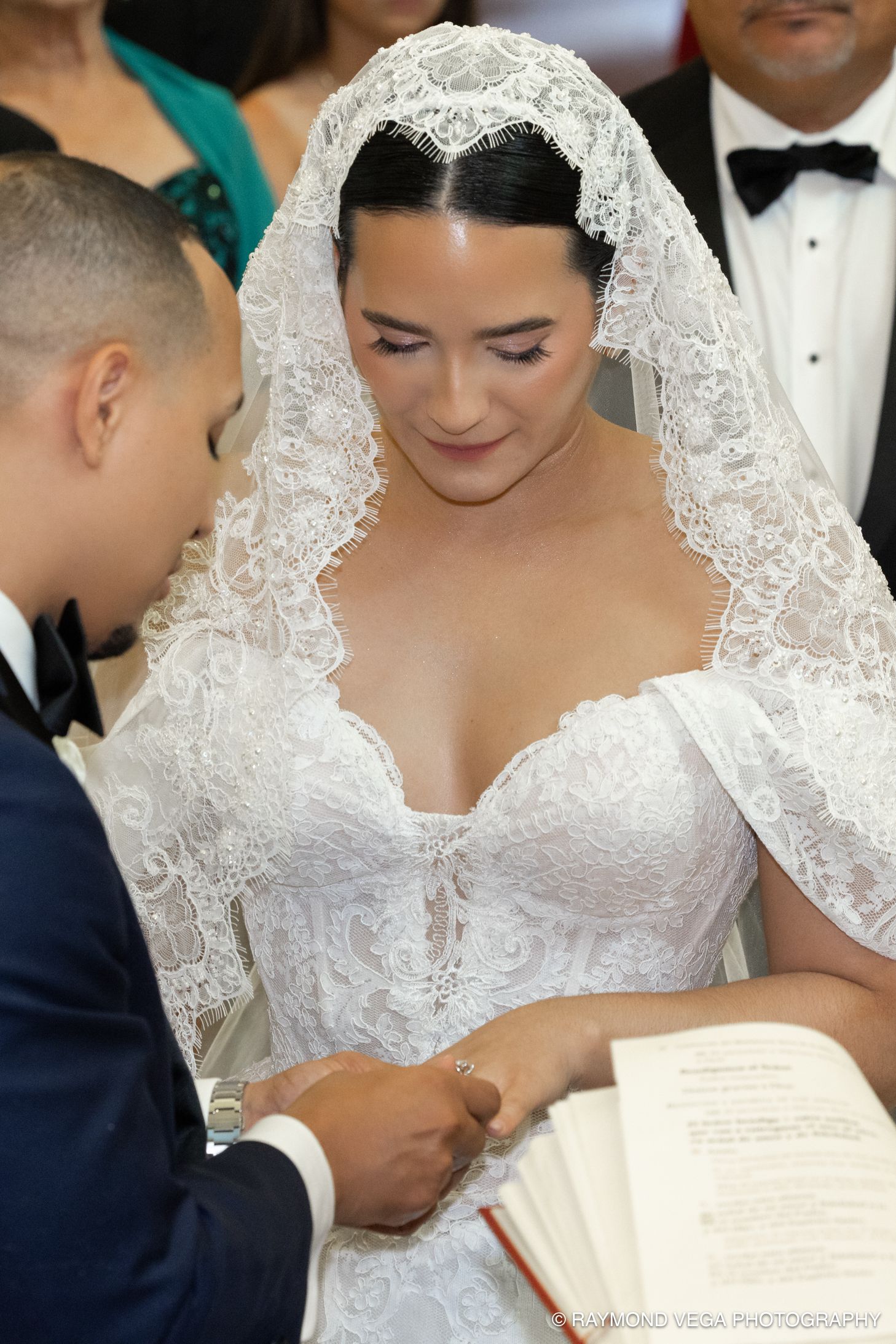 Bride in lace wedding gown and veil exchanges rings with groom during wedding ceremony.