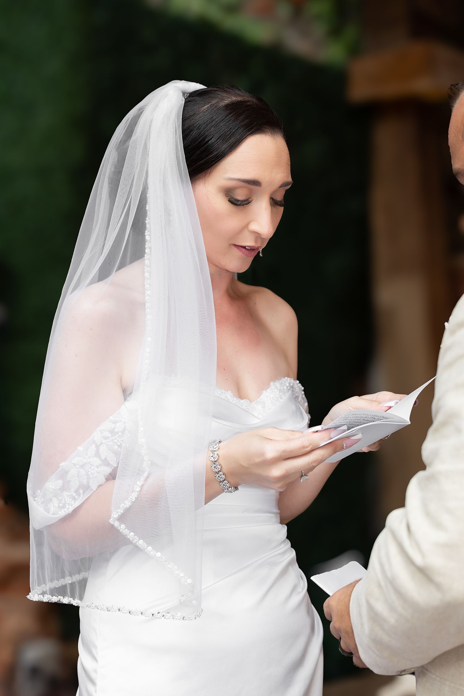 Bride in white strapless gown and veil reads wedding vows from a card during outdoor ceremony. Gallery Inn Puerto Rico
