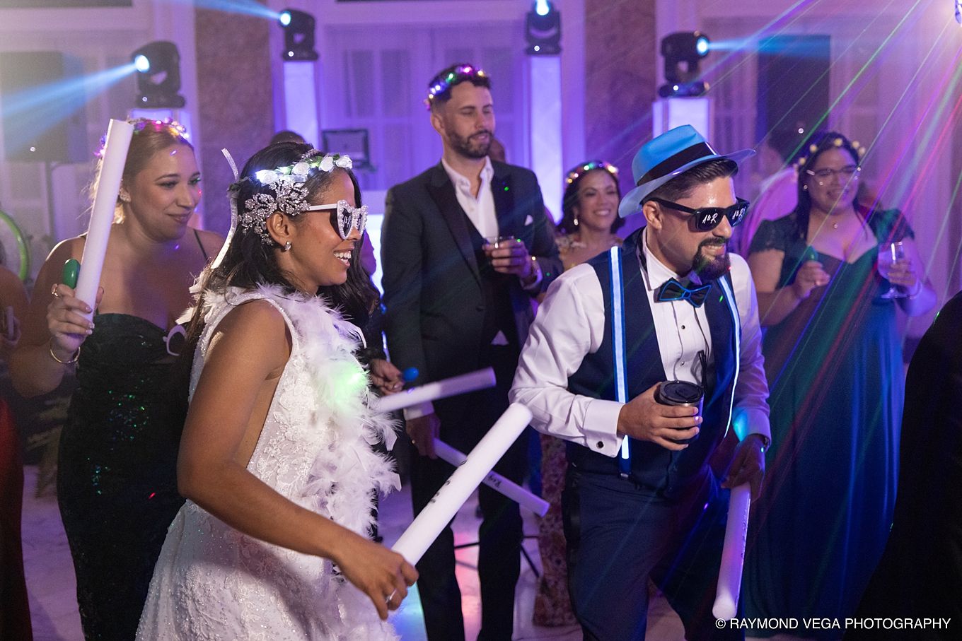 Bride and groom dancing joyfully at wedding reception with guests celebrating in background. Antiguo Casino Puerto Rico wedding