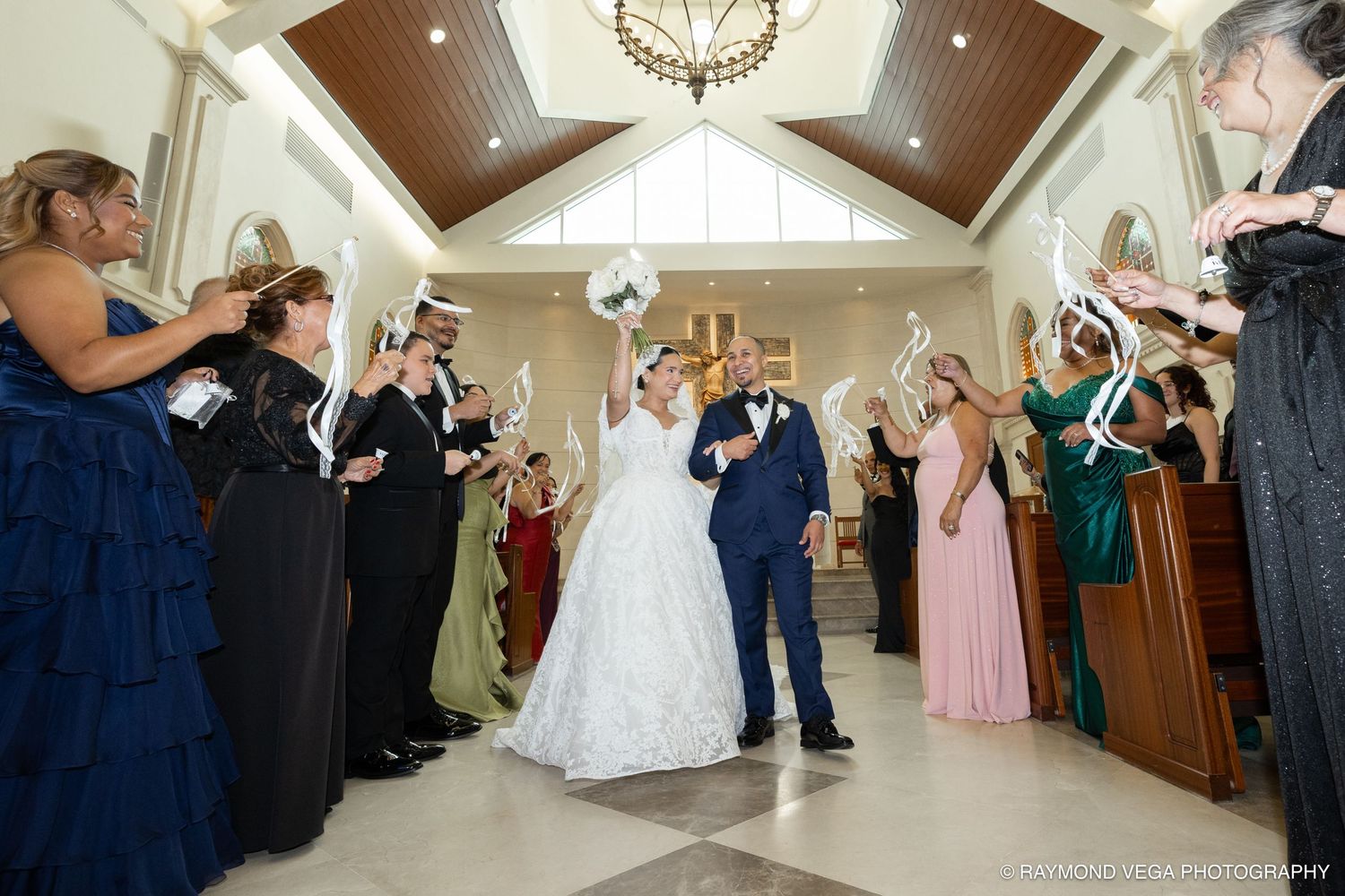 Bride and groom walk down the aisle as guests wave white handkerchiefs in a bright elegant church ceremony.