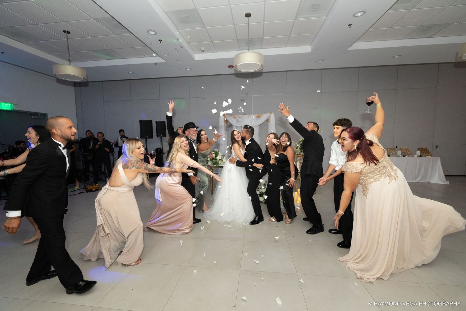 Wedding reception celebration with bride, groom, and bridesmaids dancing and throwing confetti in elegant white ballroom.