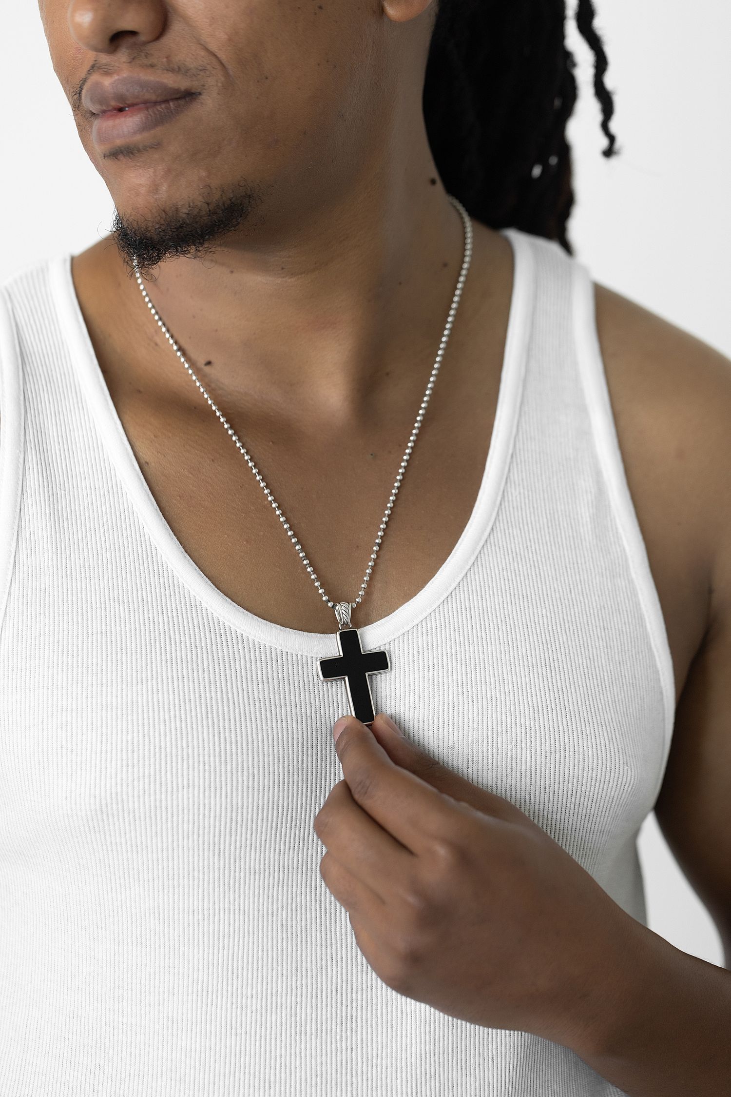 Young Black man in white tank top holding a black cross pendant necklace on a silver chain. groom wedding getting ready