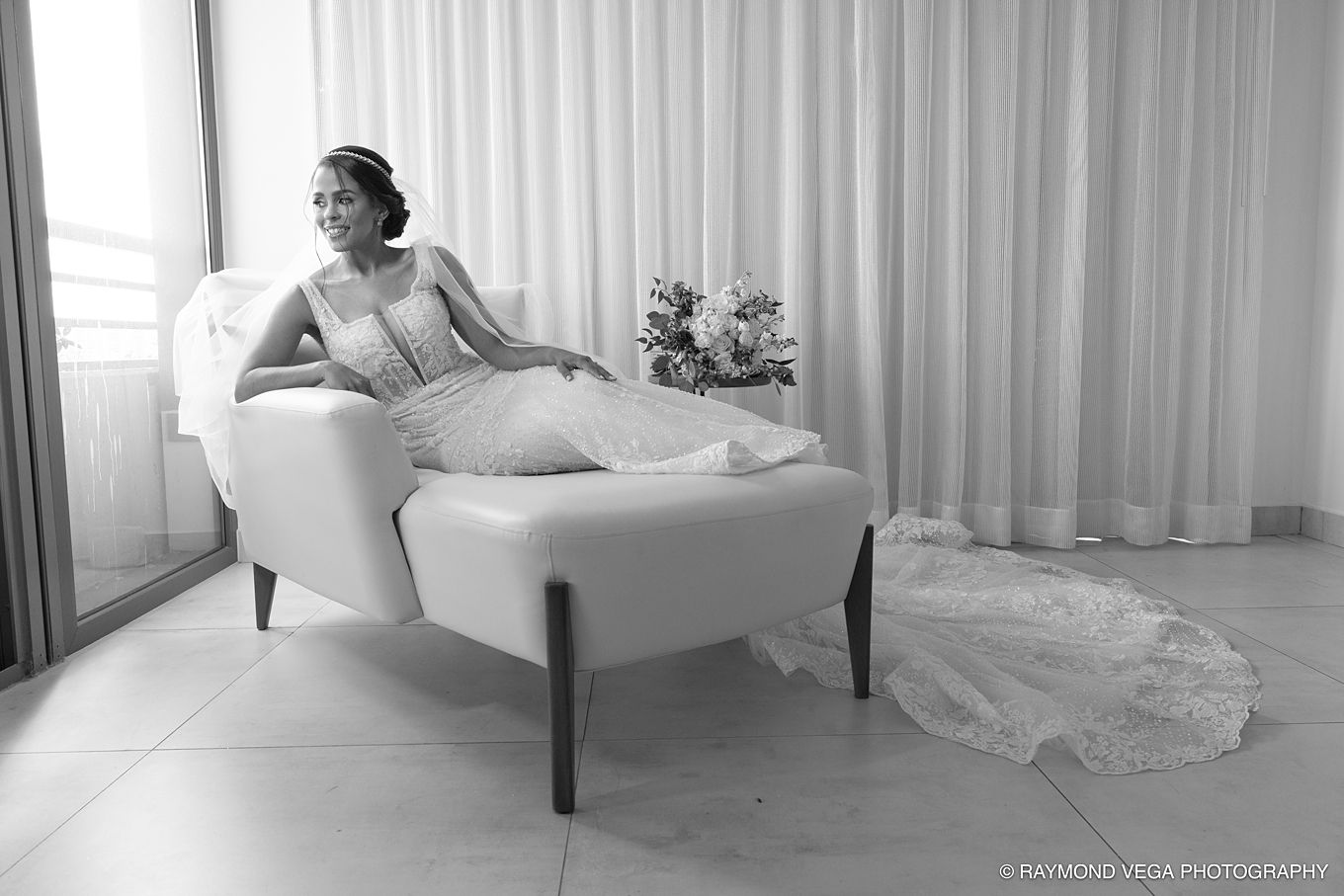 Bride in elegant wedding gown reclining gracefully on a white chaise lounge in a bright room, black and white photo. Hotel la Concha Wedding