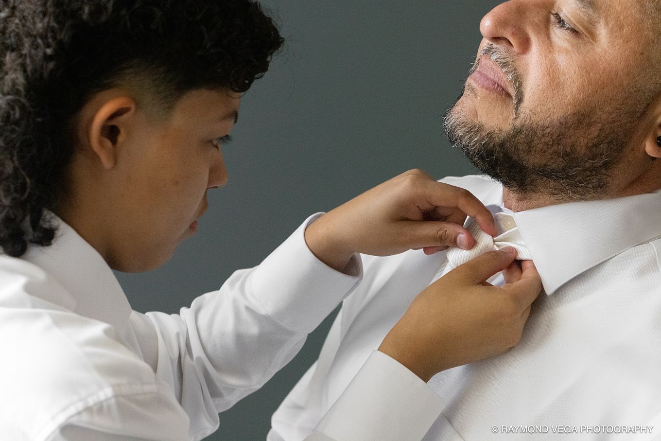 Young person helping a man button his white dress shirt collar in a professional photography setting in Courtyard by Marriott isla verde