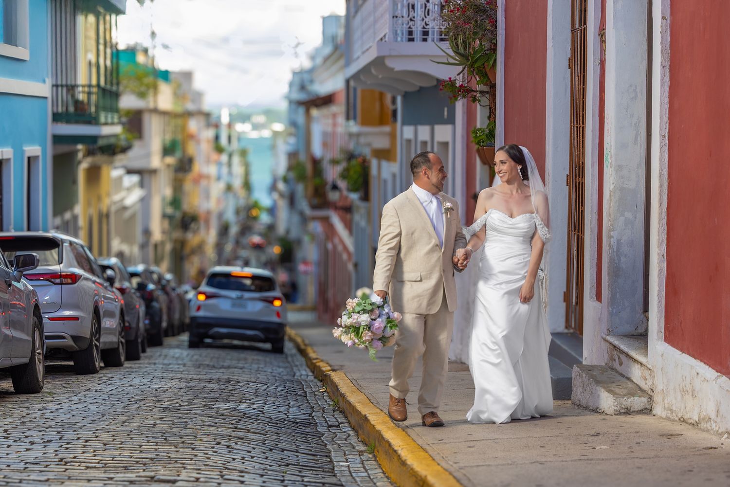 Bride and groom walking hand-in-hand on a cobblestone street in Old San Juan, Puerto Rico, with colorful buildings.