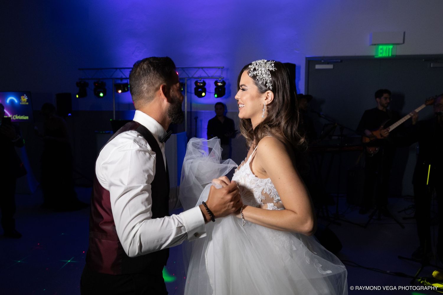 Bride and groom share their first dance at a wedding reception with blue lighting and a live band performing in the background.