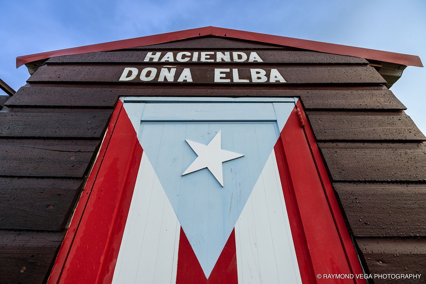 Hacienda Doña Elba building facade featuring a painted Puerto Rican flag with red, white, and blue triangle with star.