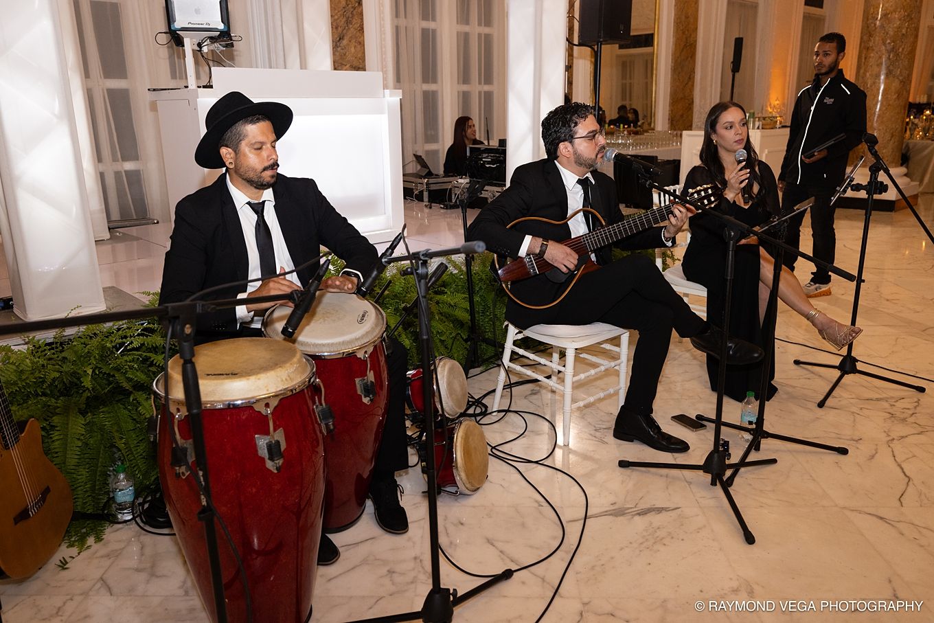 Live band performing at elegant event, featuring conga drums, guitar, and clarinet players in formal attire.