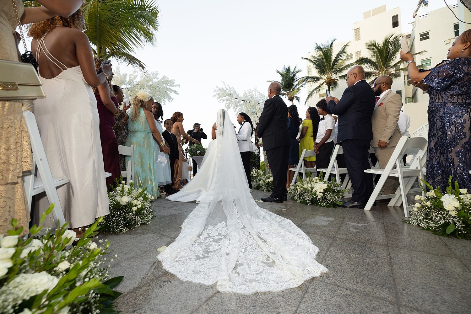 Wedding guests seated outdoor ceremony La Concha Resort Puerto Rico with white floral arrangements.
