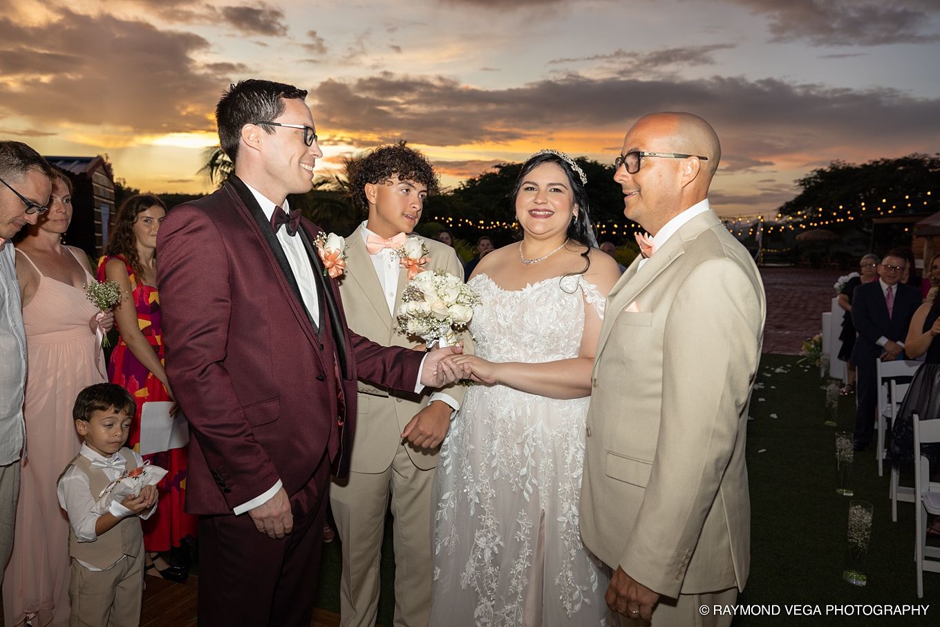 Bride and groom share a joyful moment with guests during an outdoor wedding ceremony at sunset.