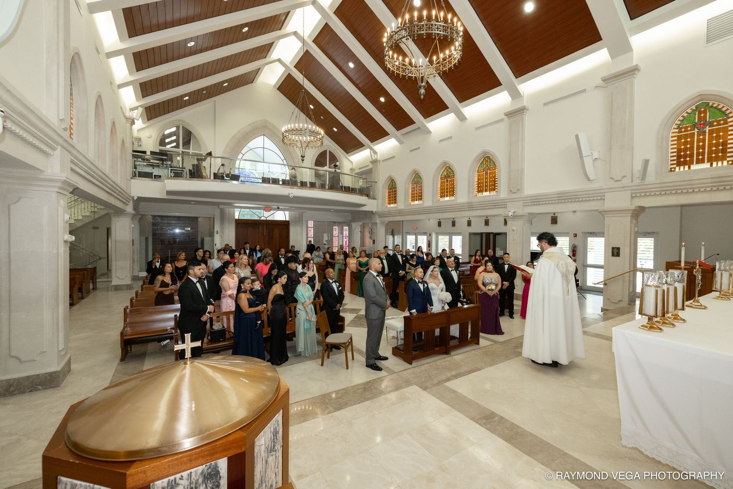 Guests gather in a bright, modern church for a wedding ceremony, with the officiant standing at the altar.