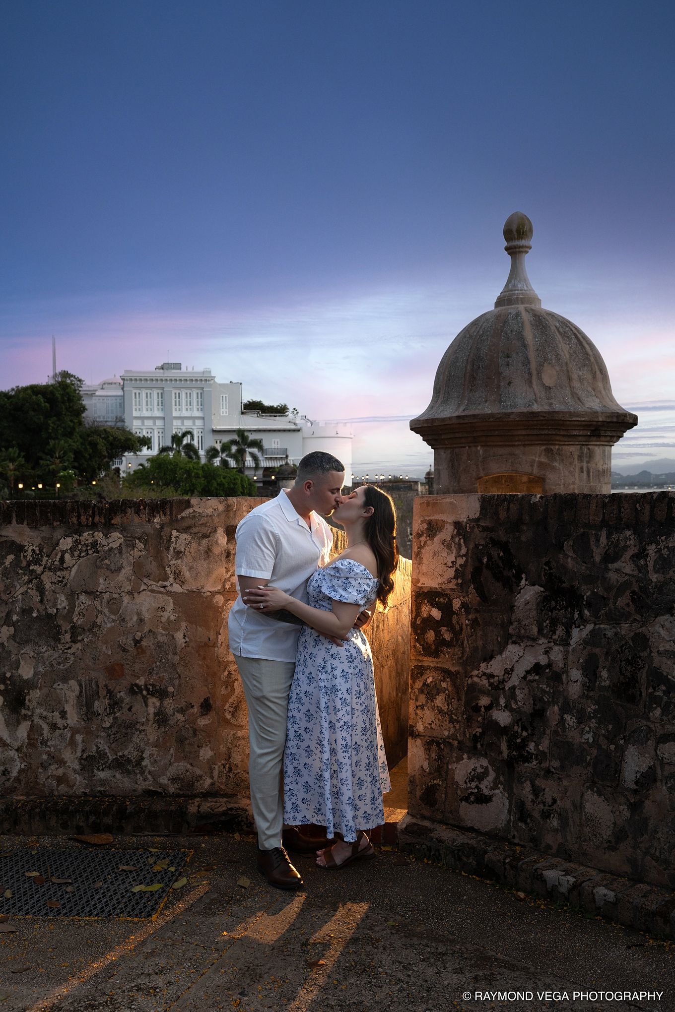 Couple sharing a romantic kiss at sunset near a historic stone wall and sentry tower in Old San Juan, Puerto Rico. - Love Story