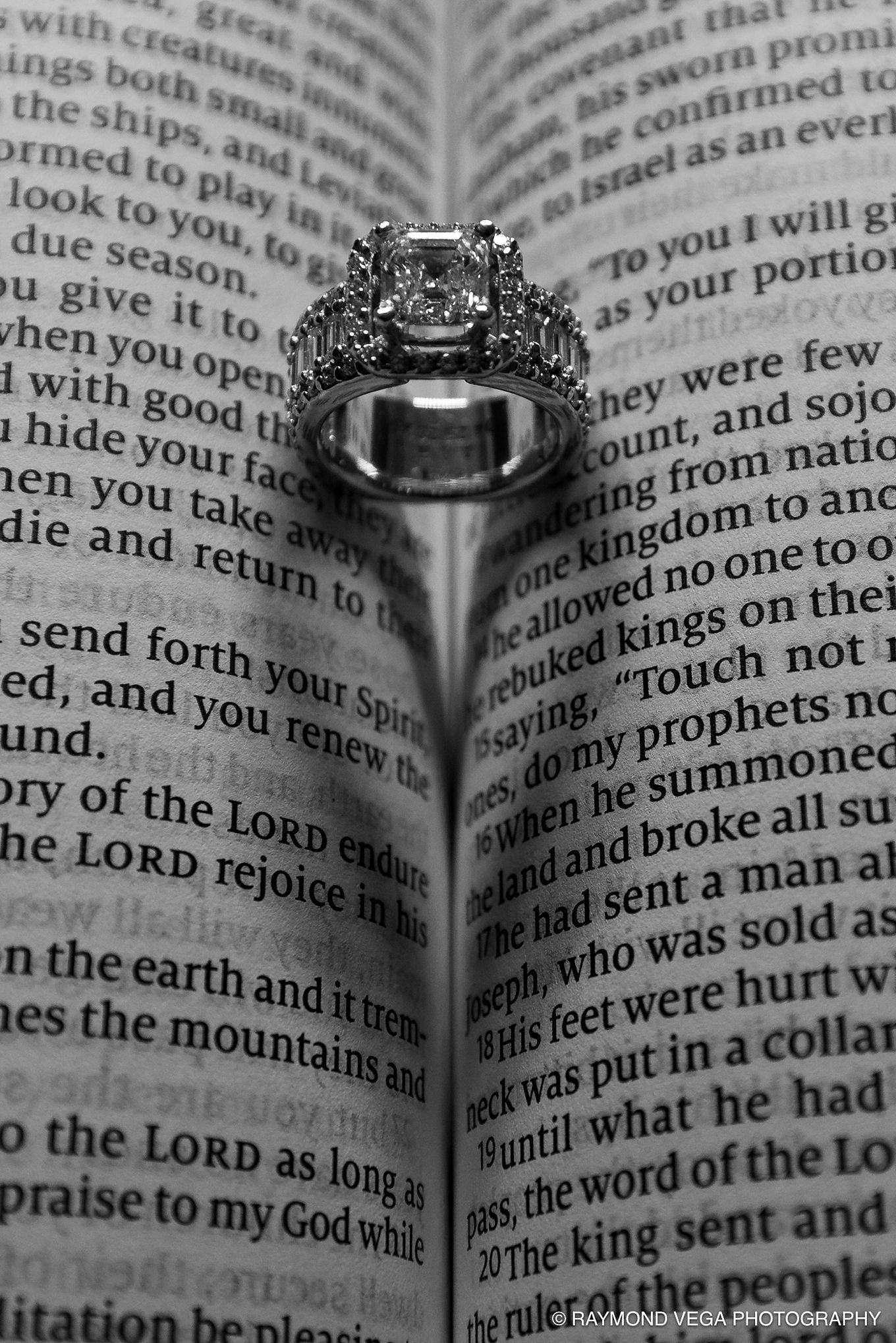 Diamond engagement ring casting a heart shadow on an open Bible page, black and white wedding photography.