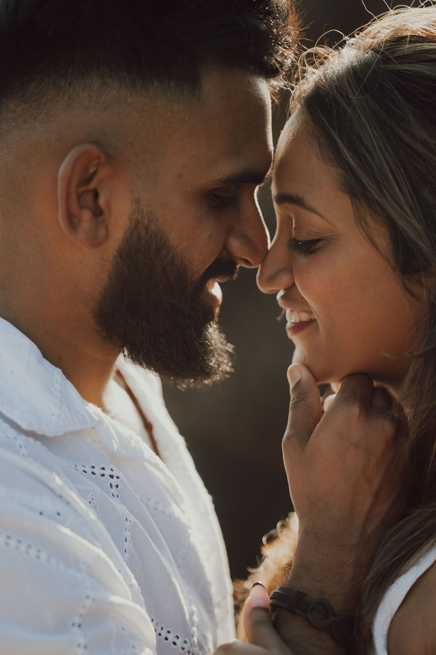 A romantic couple in white clothing share an intimate moment in a series of close-up portraits with dramatic lighting.