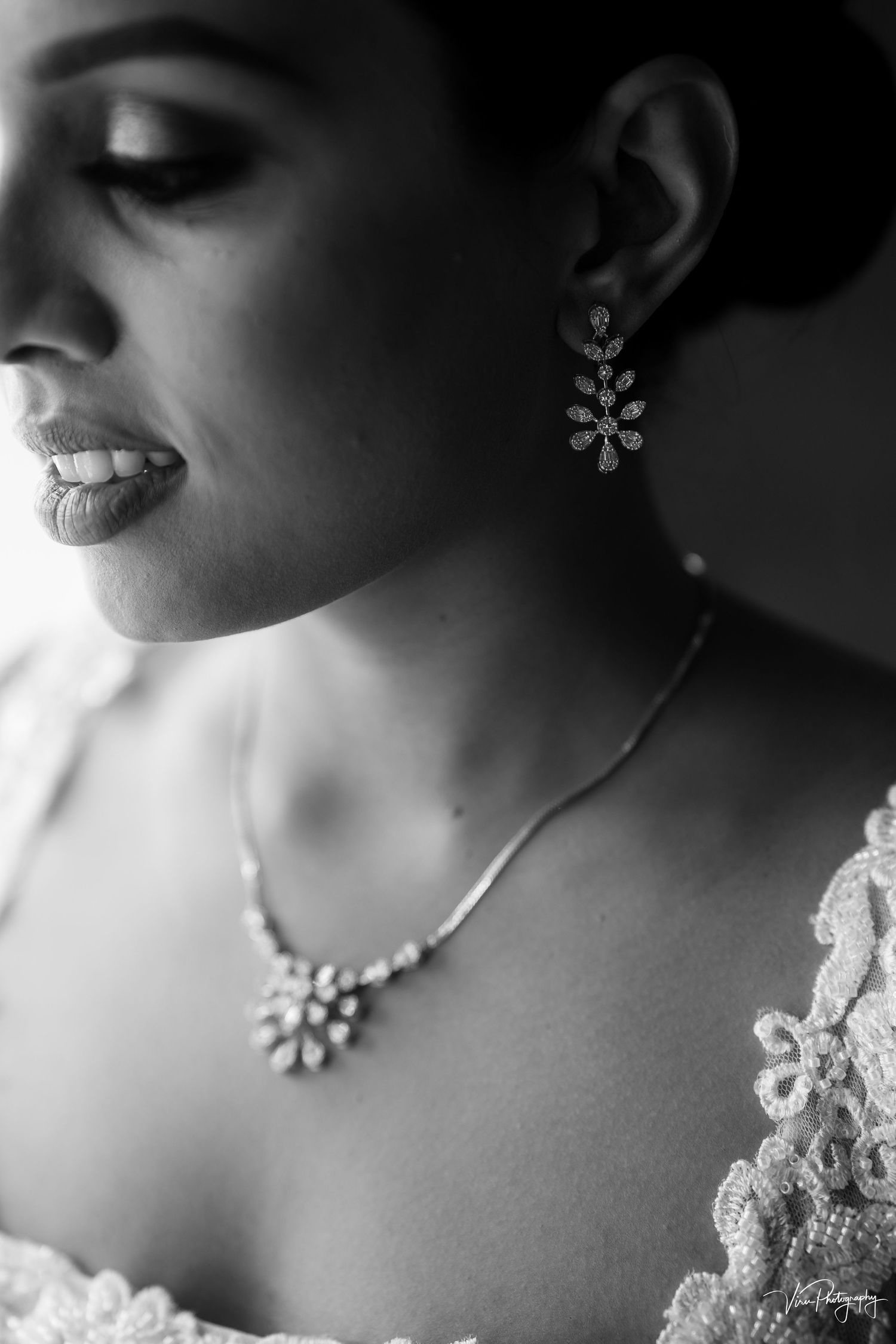 Black and white close-up shows elegant bridal jewelry with floral earrings and necklace against white lace dress details.