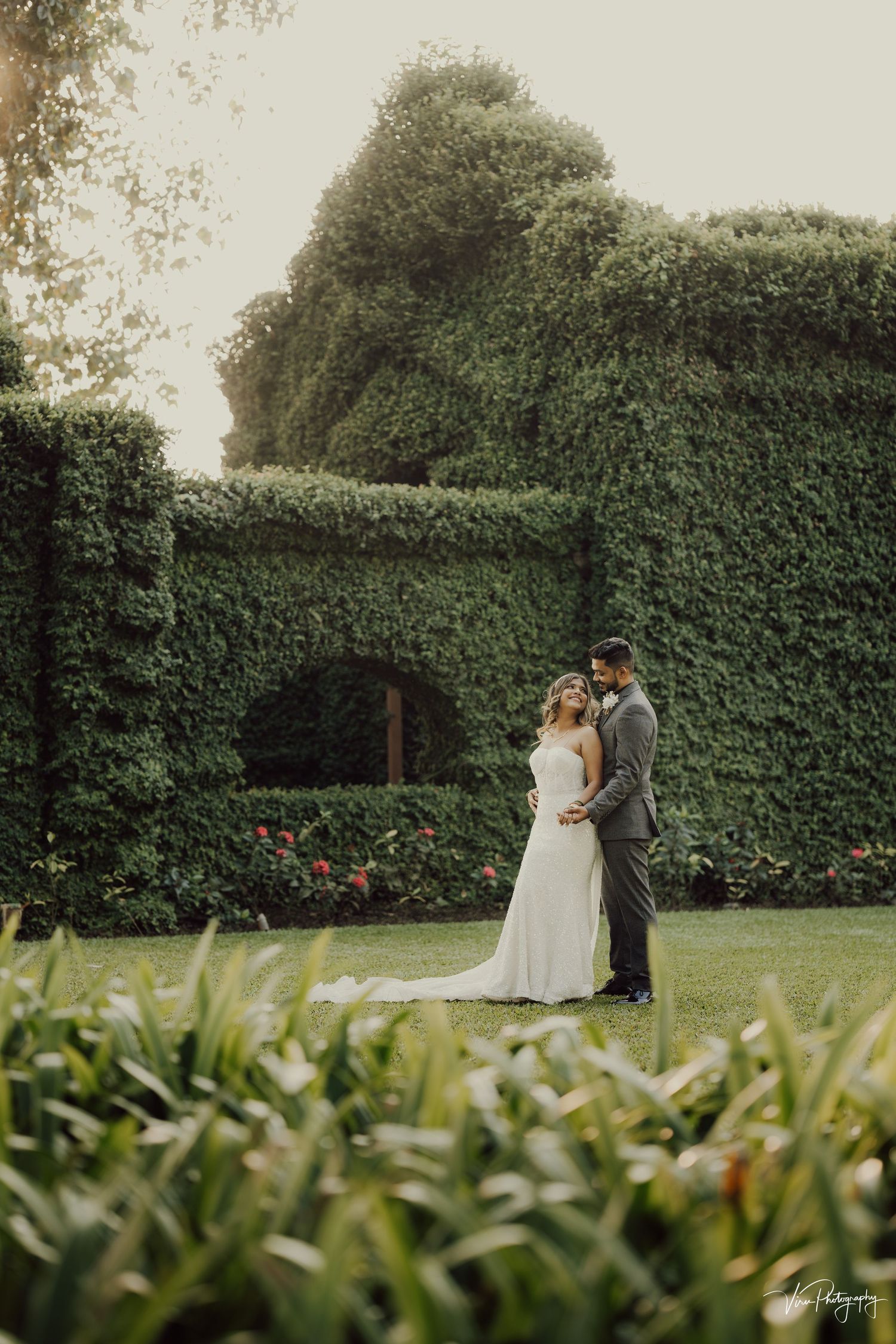 A romantic wedding moment captured in a garden with towering ivy-covered walls and lush greenery creating an enchanting backdrop.