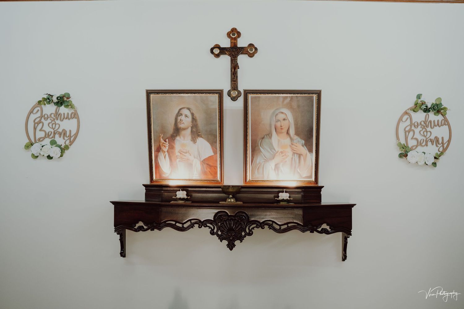 Brown wooden decorative wall shelf with religious portraits and cross mounted between matching floral wall decor.