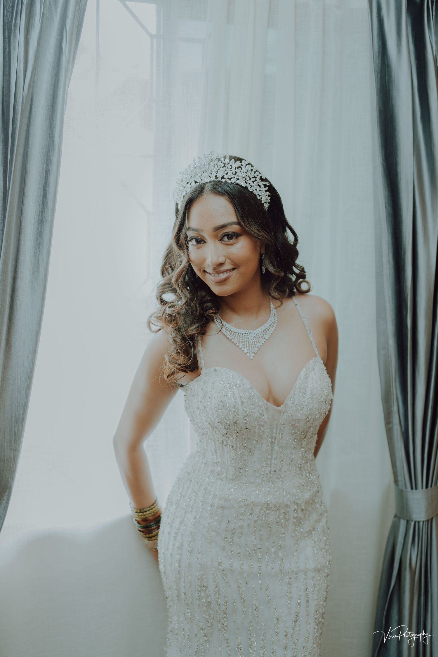 Elegant bride wearing a sparkling white fitted wedding dress with sweetheart neckline, crystal crown and curled hair.