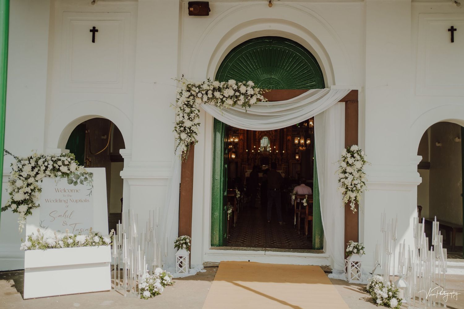 Elegant church entrance decorated with white floral arrangements and candles for a wedding ceremony.