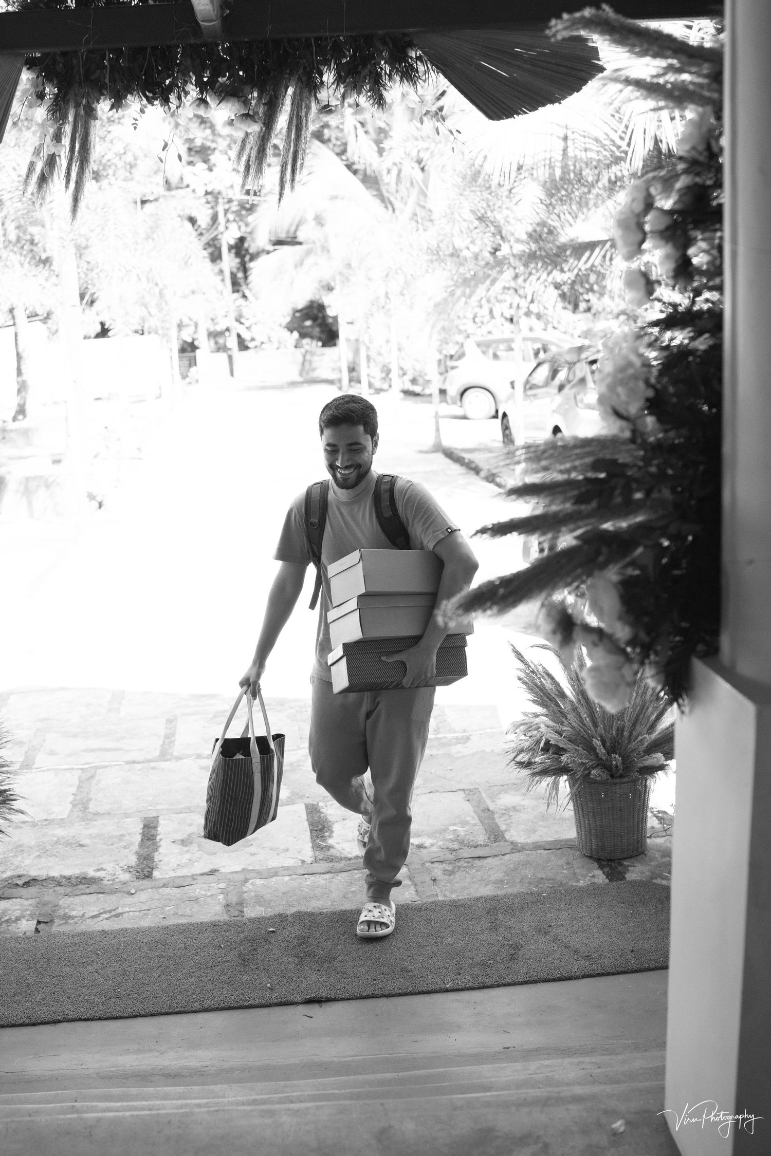 A person carrying multiple boxes and a shopping bag walks up outdoor steps in a black and white photograph.