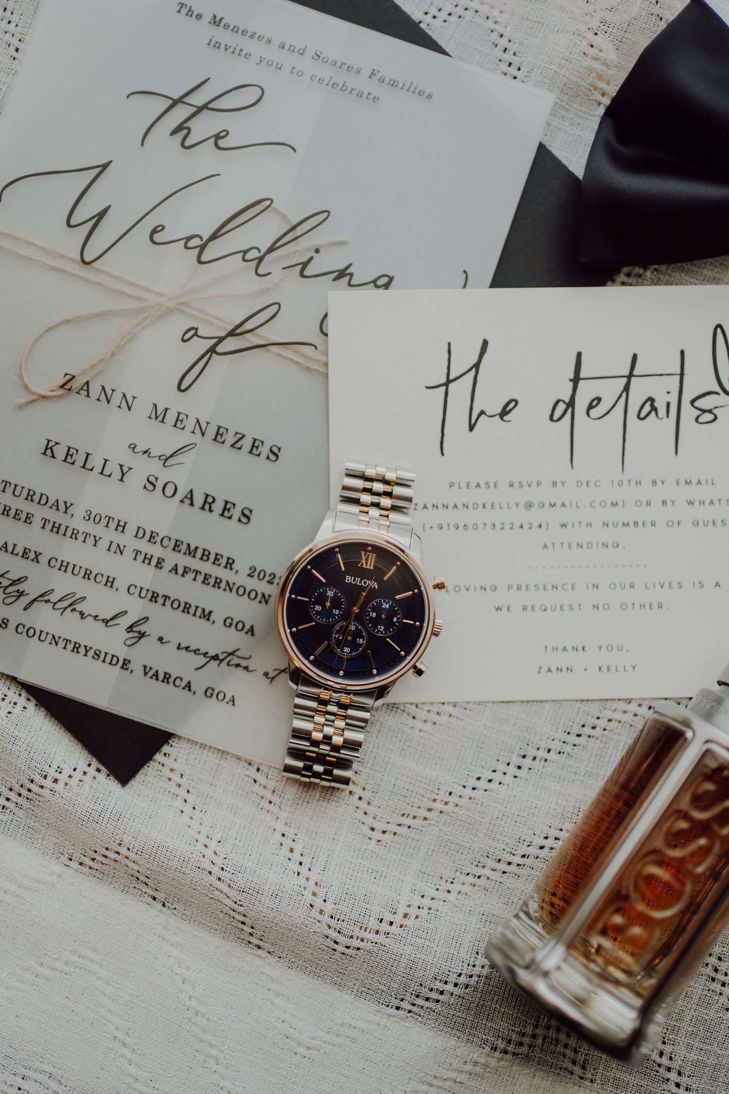 Wedding invitation details with luxury watch and perfume bottle styled on white surface.
