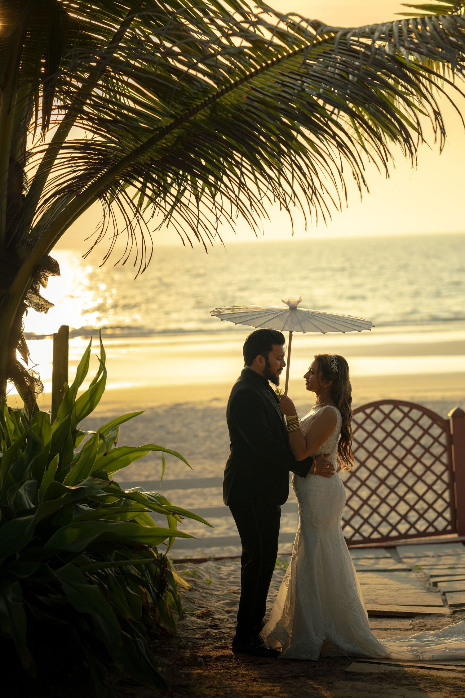 A romantic sunset beach wedding ceremony silhouetted against palm trees and golden sky.