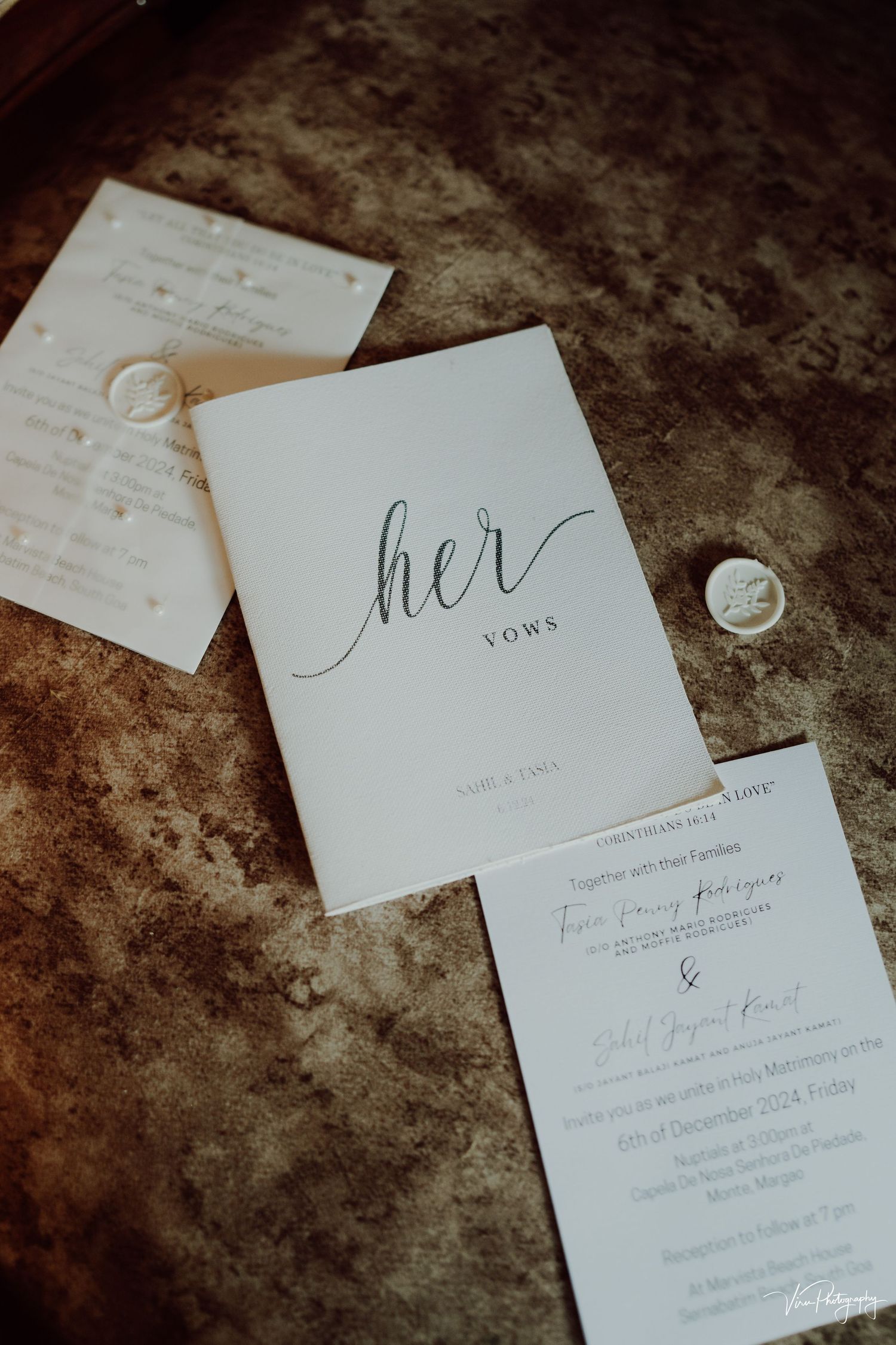 Wedding stationery including a 'her vows' booklet and invitations laid on a textured brown surface.