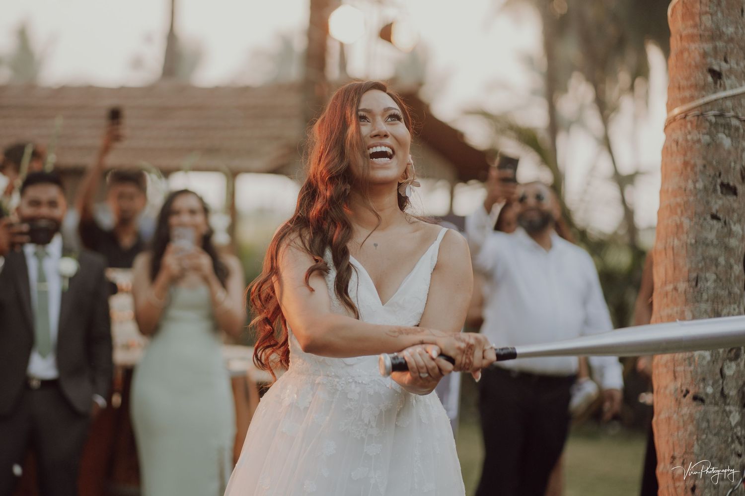 A bride laughs joyfully while holding a sparkler during an outdoor evening wedding celebration.