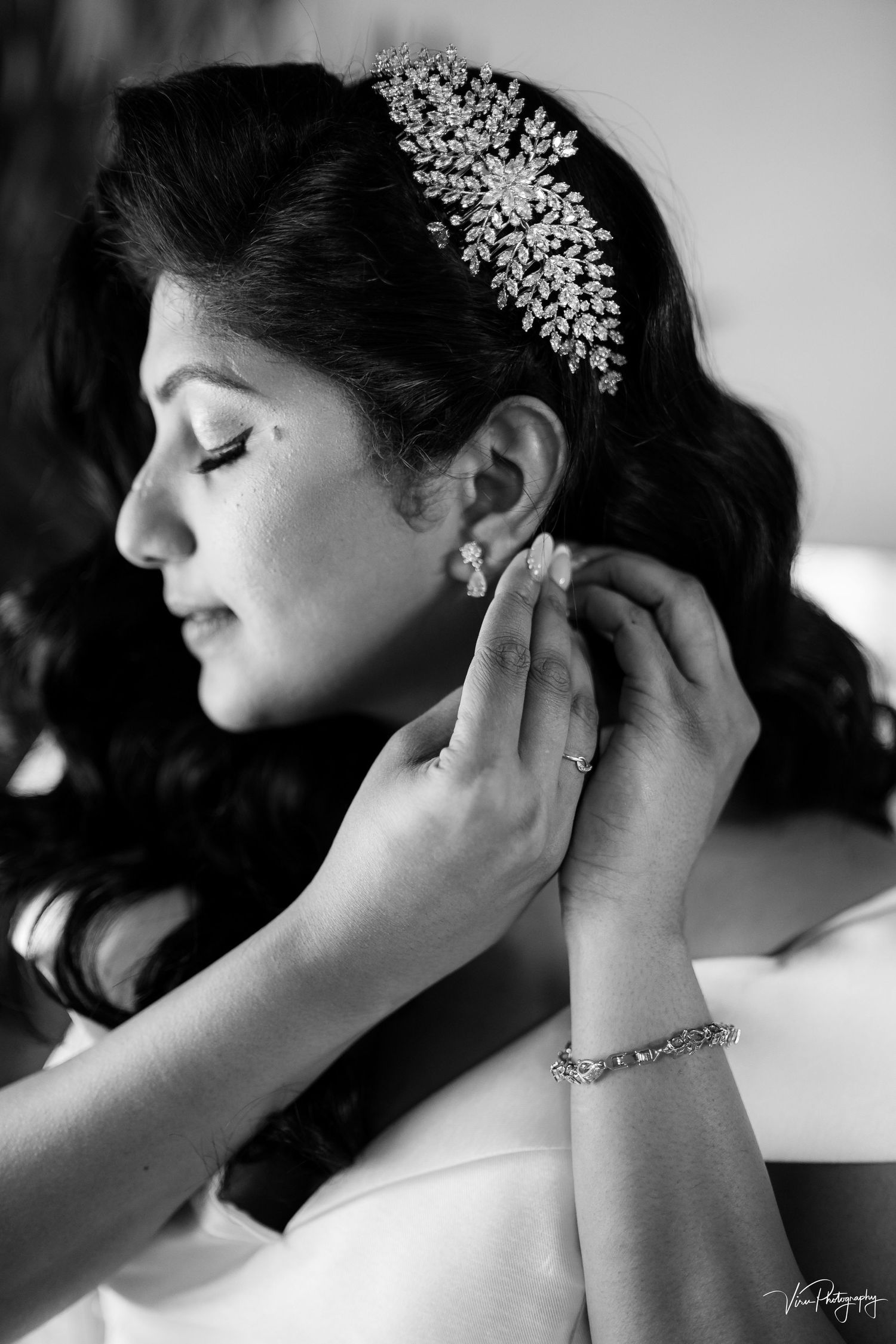 A black and white bridal portrait showing elegant crystal hairpiece, earrings and jewelry accessories during preparation.