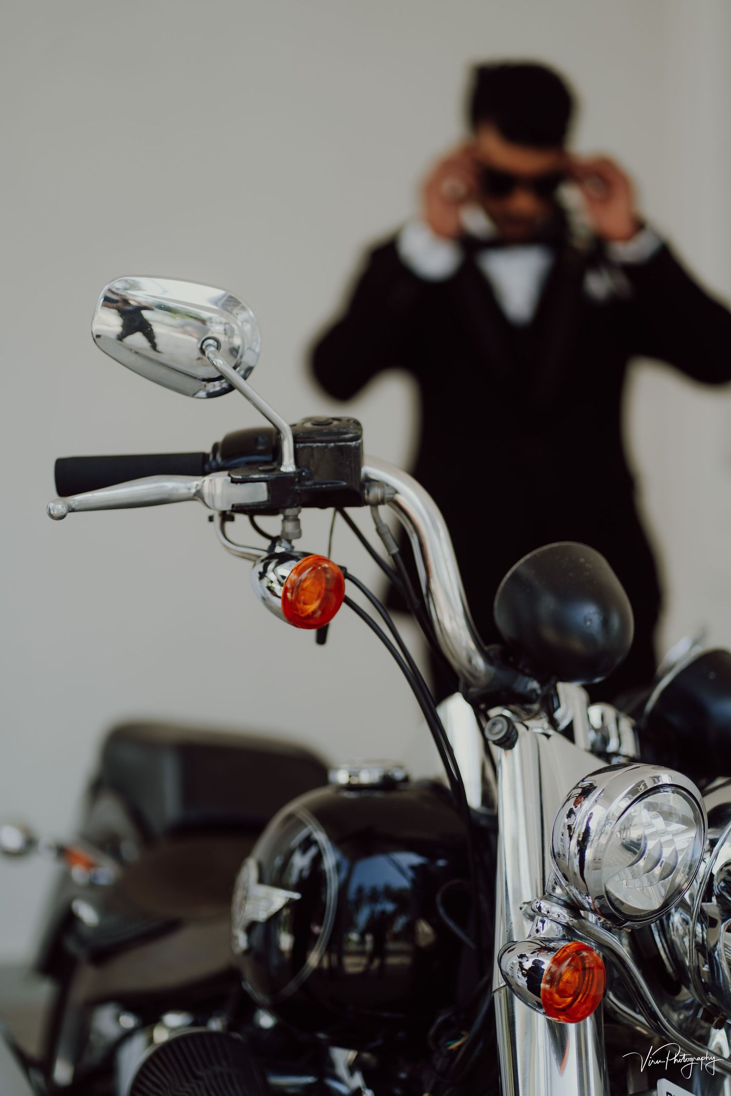 Close-up view of a motorcycle handlebar with chrome mirrors and controls, with a silhouetted figure in the background.