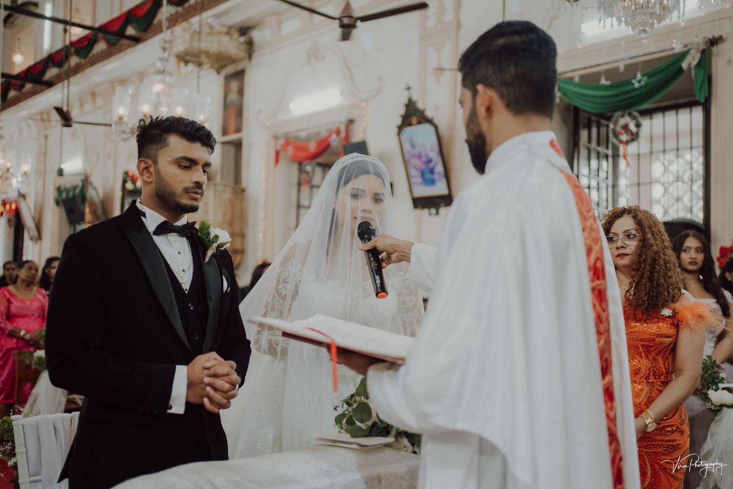 Wedding ceremony taking place inside a church with priest and groom in formal attire at the altar.