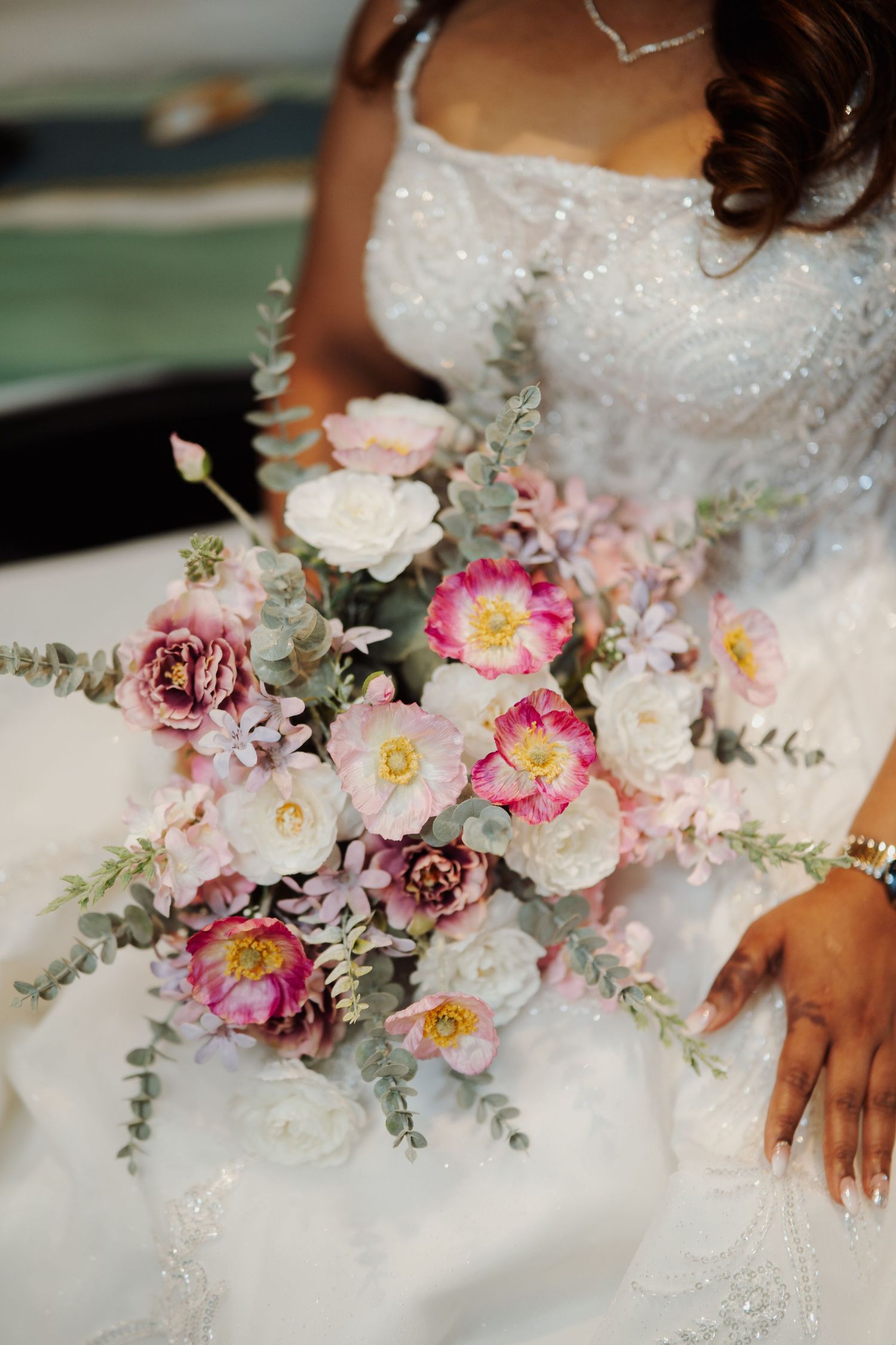 Beautiful bridal bouquet featuring pink and white roses with silvery eucalyptus leaves against a white beaded wedding dress.
