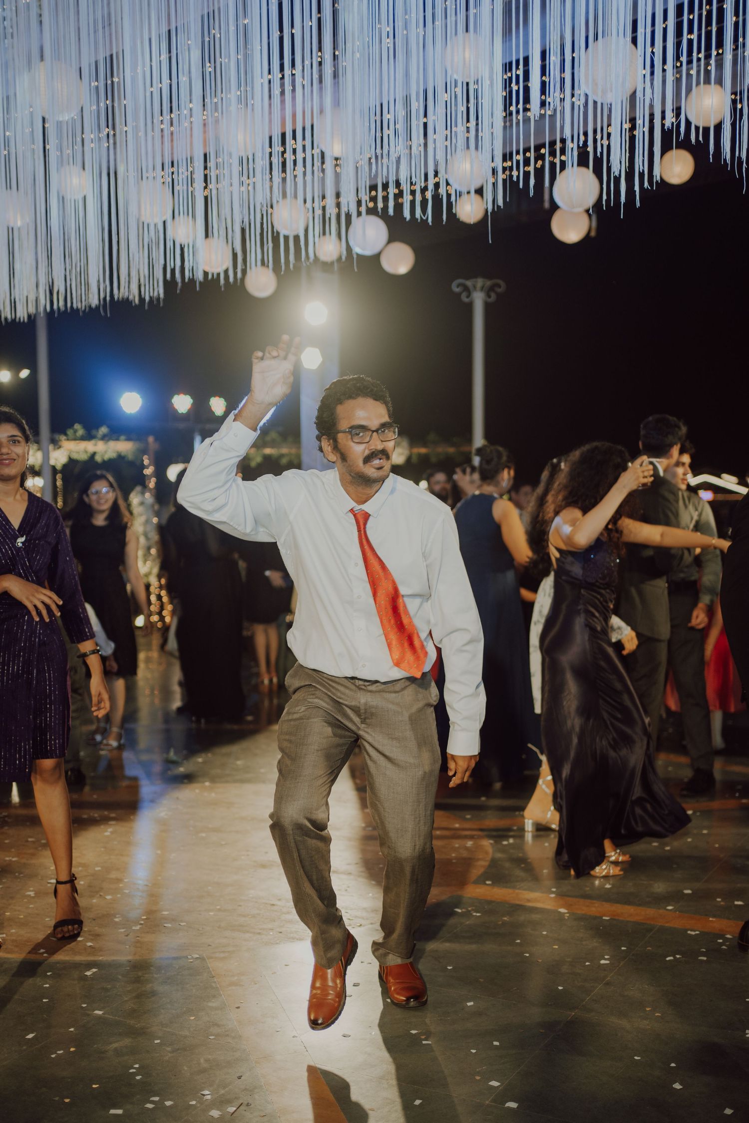 Wedding guest dances enthusiastically under decorative string lights at reception.