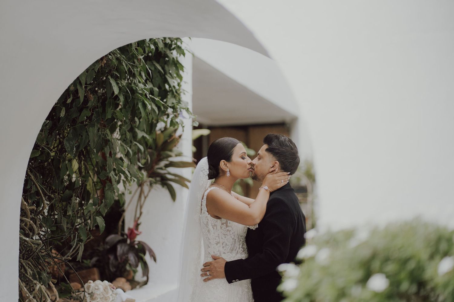 A romantic wedding moment framed by a white archway with greenery.