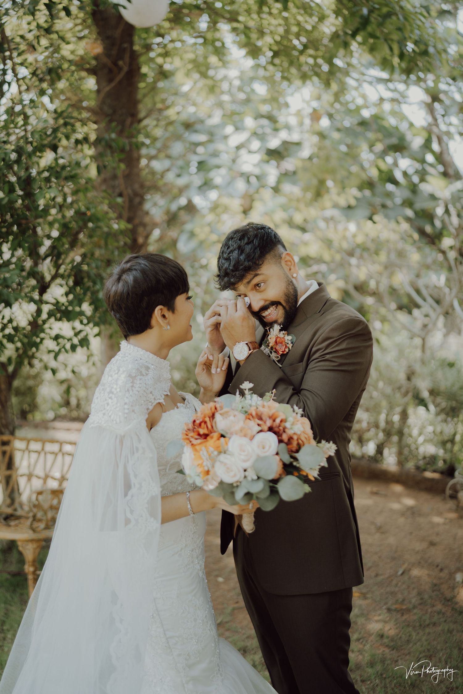 Emotional wedding scene with couple sharing a touching moment surrounded by greenery in outdoor garden setting.