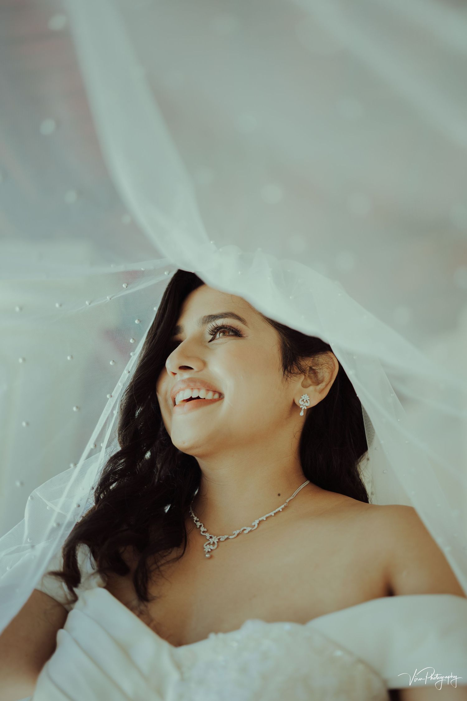 A serene portrait of a bride in a white wedding gown and delicate veil, smiling with joy.