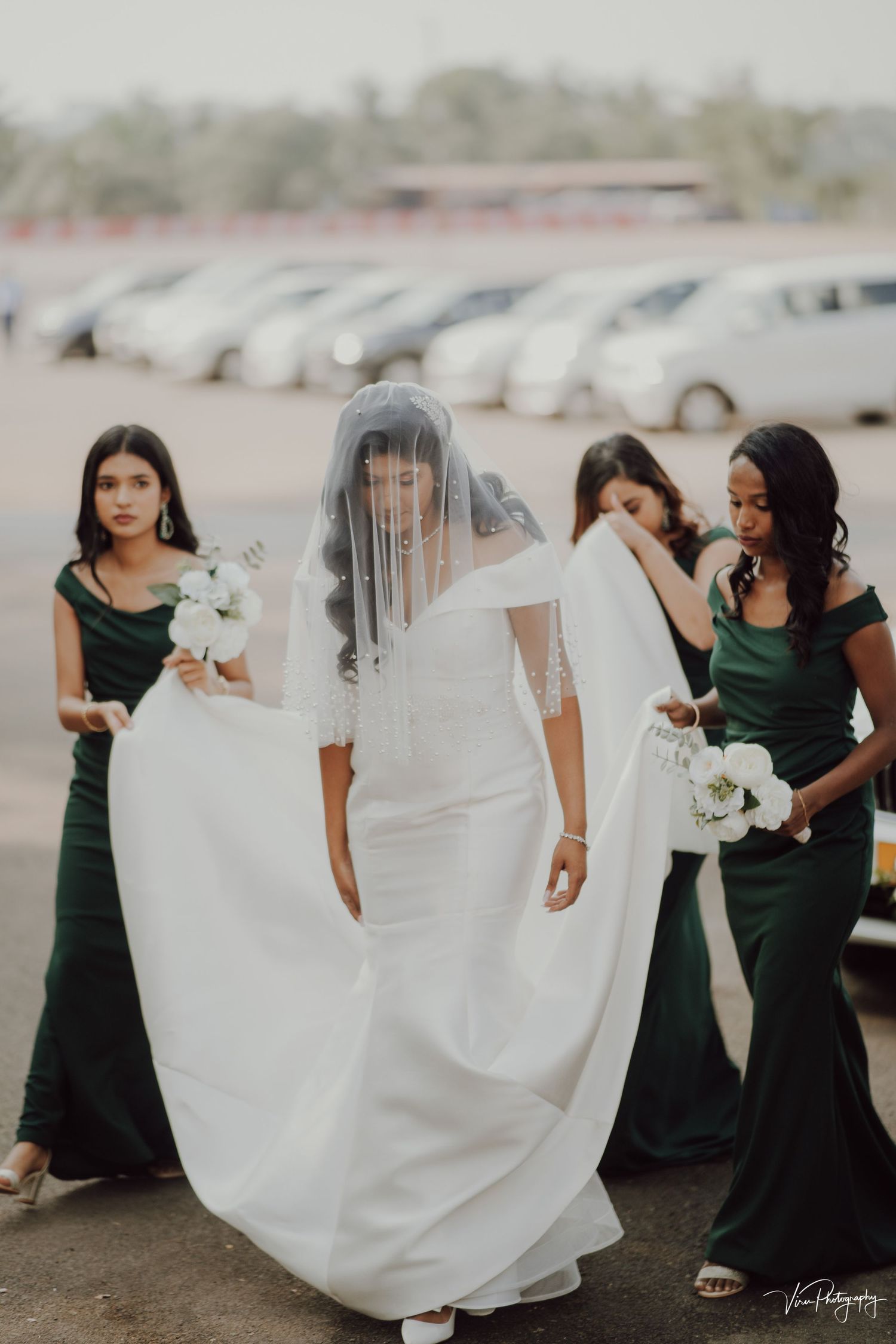 Wedding party in emerald green bridesmaid dresses walking together as bride wears flowing white gown with veil.