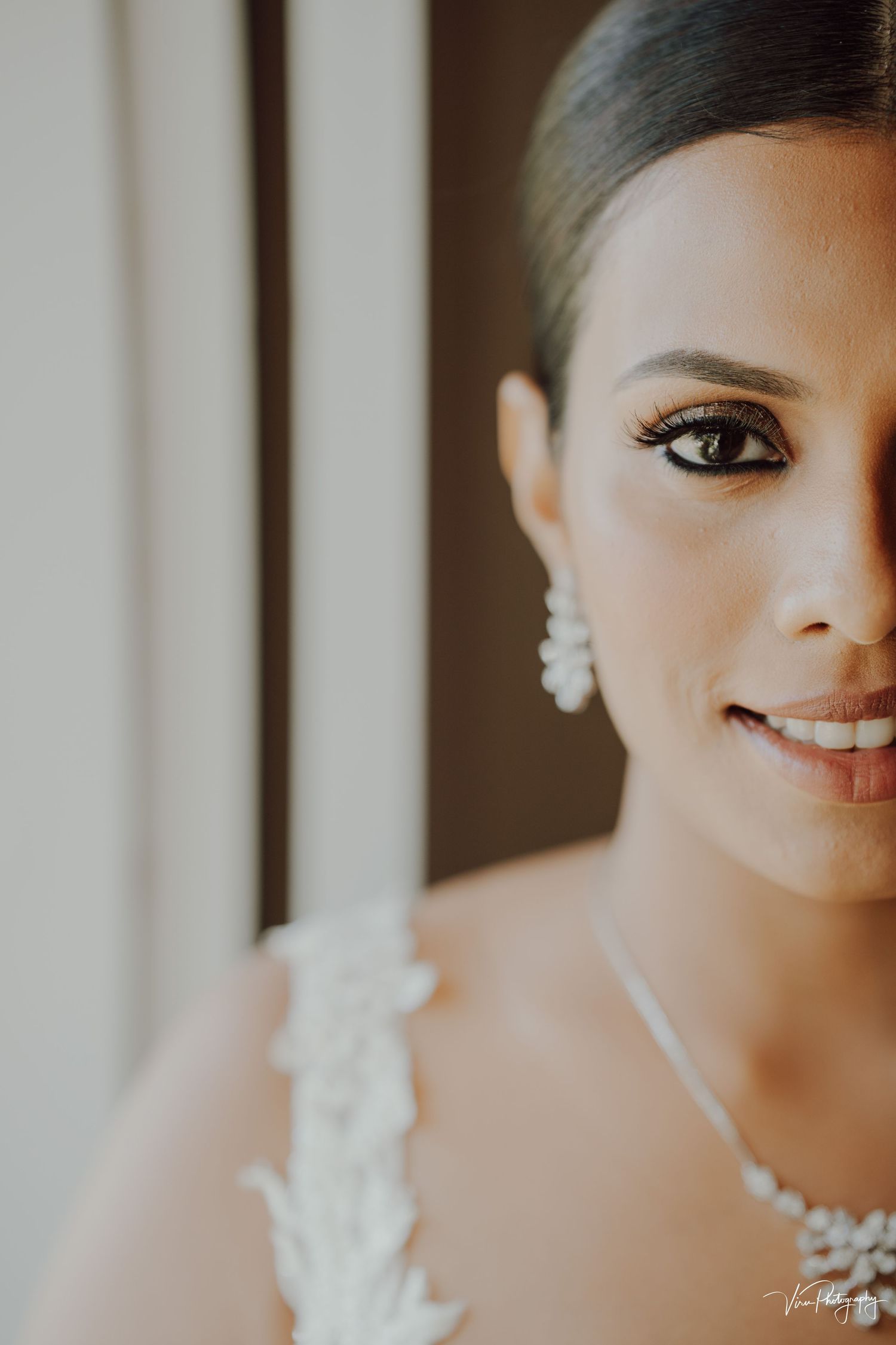 Close up portrait of someone wearing bridal attire with delicate lace details, pearl necklace and earrings in soft lighting.