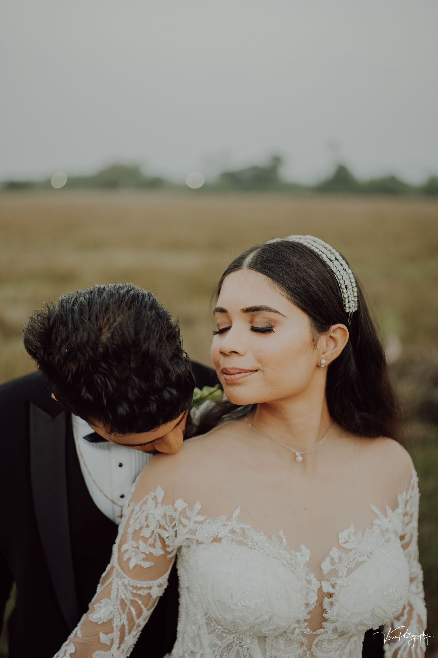 A romantic wedding portrait in a field at sunset with the bride wearing a lace dress and delicate headband.