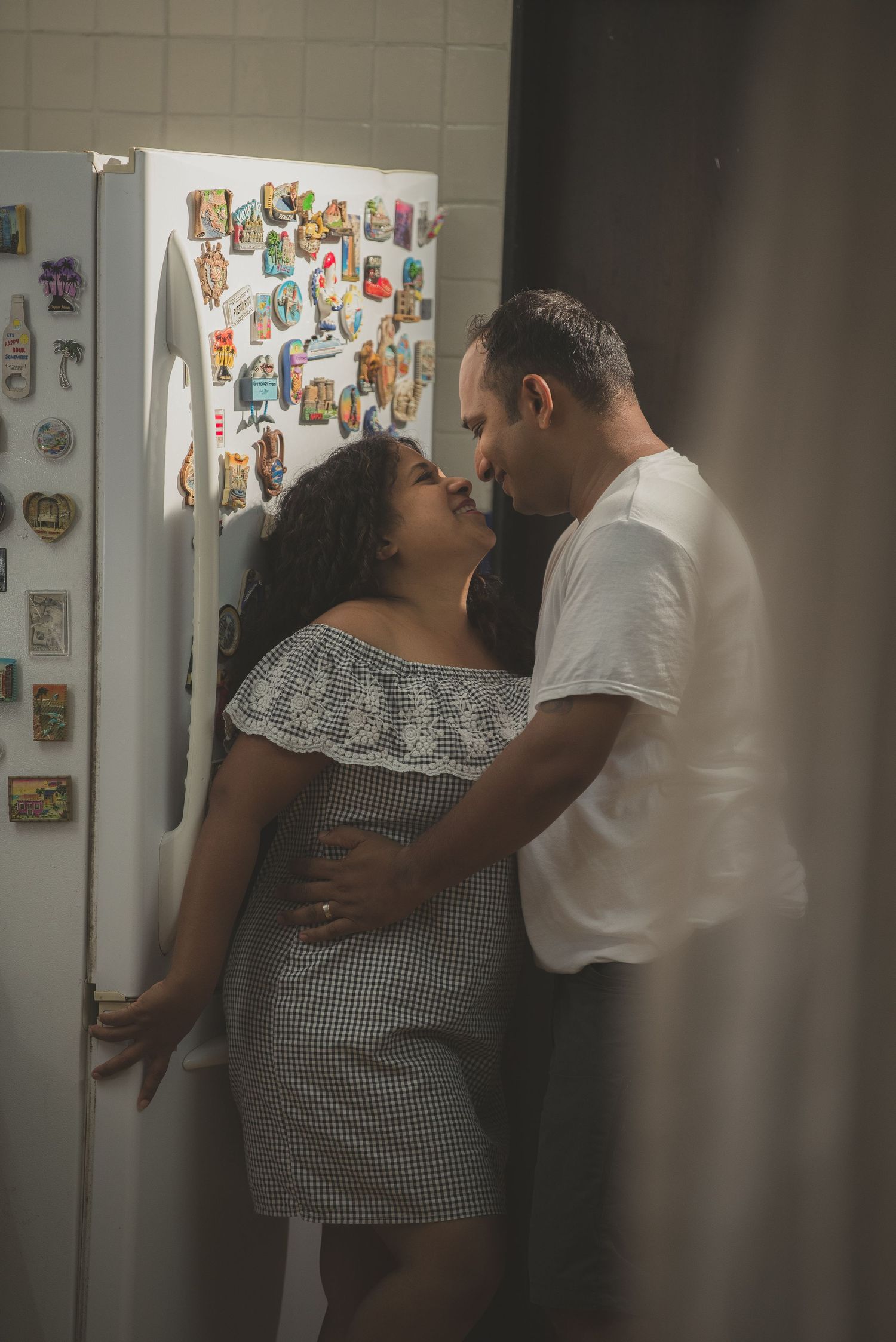 Romantic couple embracing in front of refrigerator covered with colorful magnets in kitchen setting.