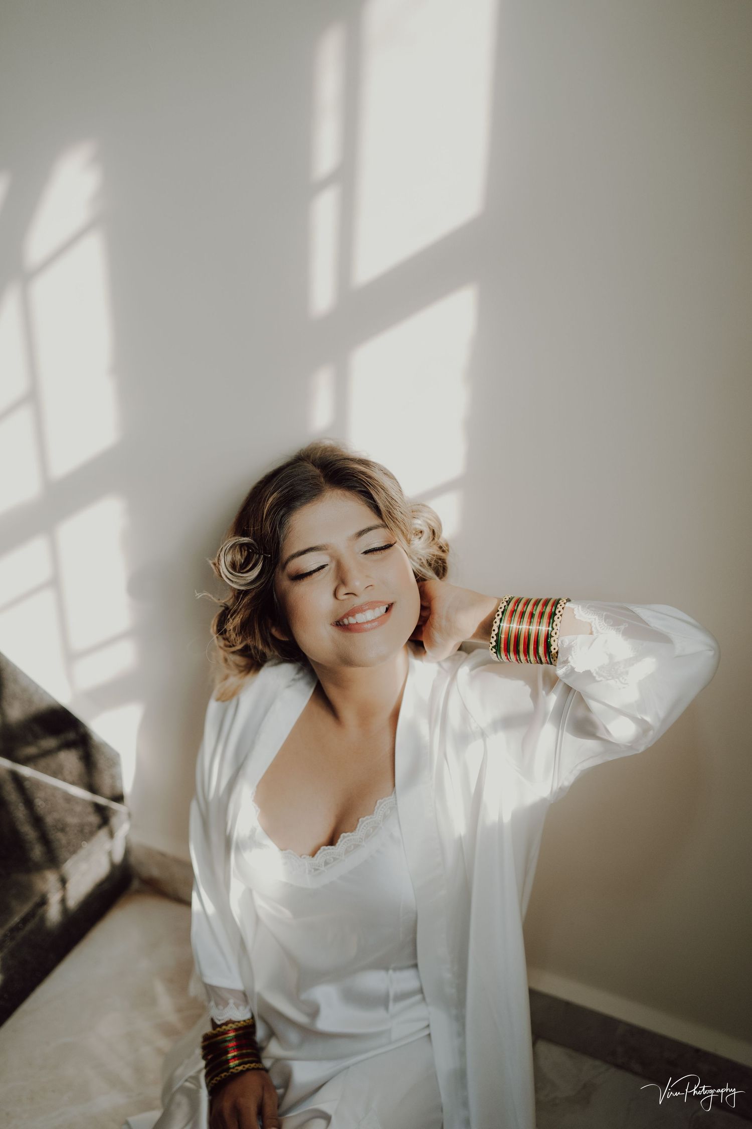 A romantic boudoir photo features soft window light casting shadows while someone poses in white silk attire.